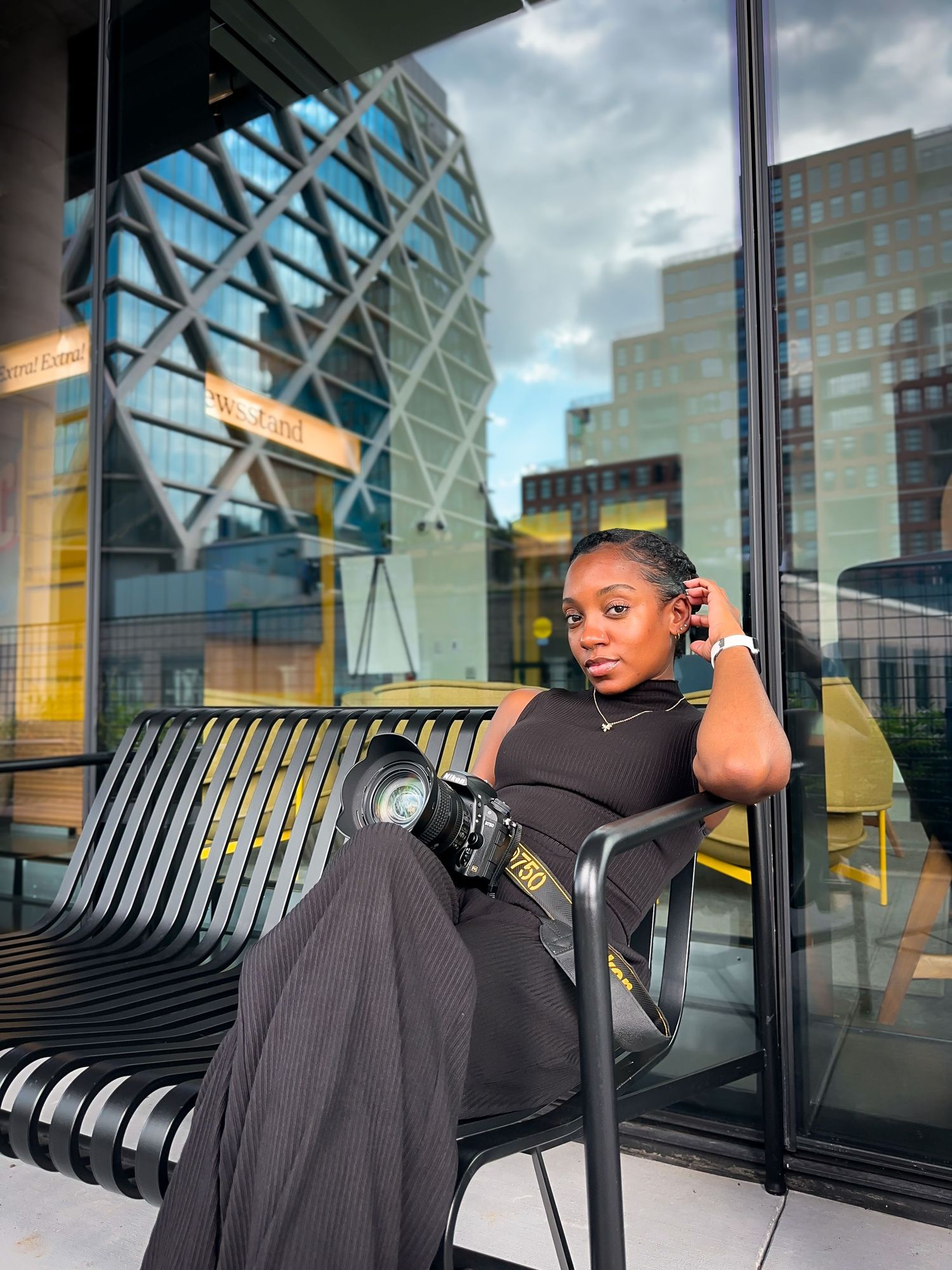 White romper figure poses playfully on modern metal bench against glass building.