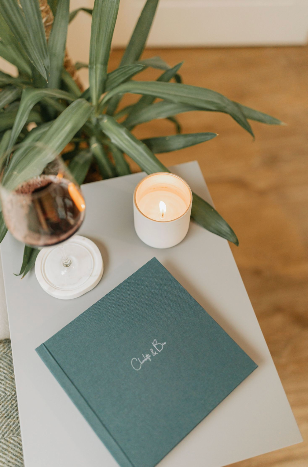 A lit white candle holder sits beside stacked books and an open notebook with handwritten text on a white surface.