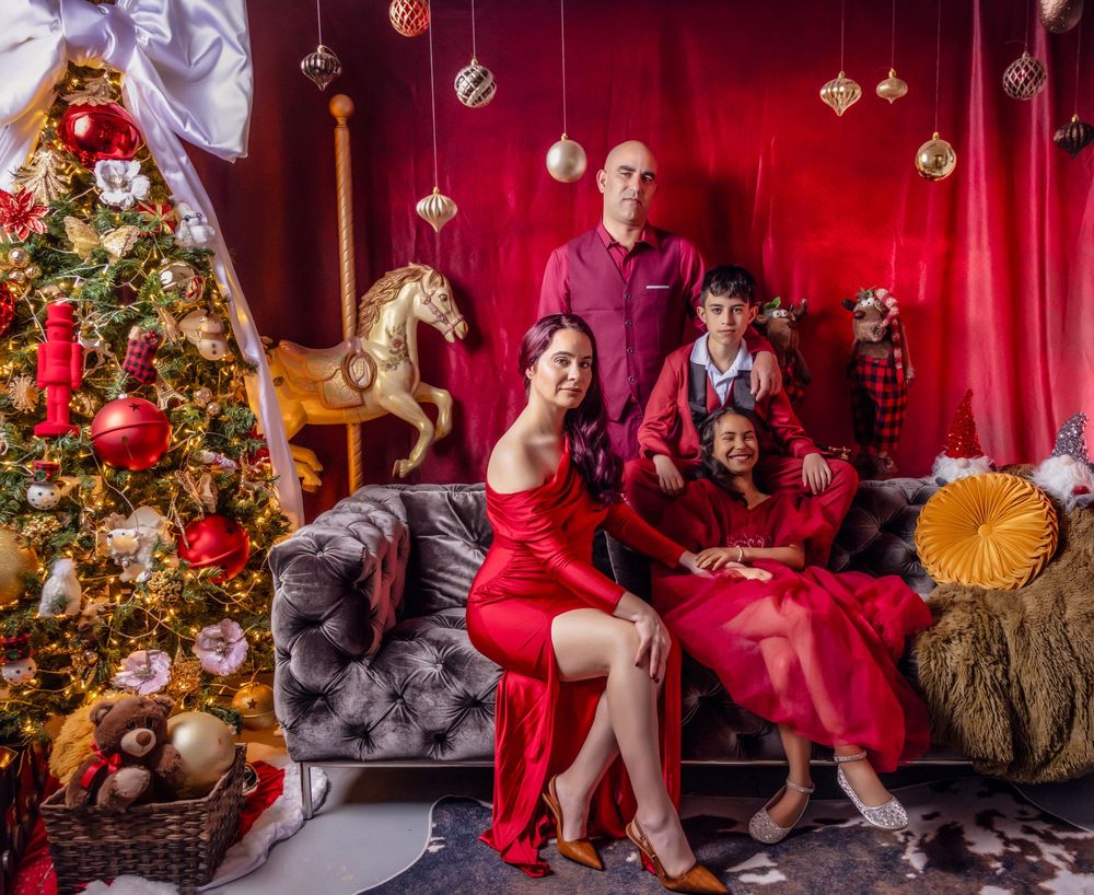 Festive holiday scene with decorated Christmas tree, red backdrop, ornaments, and people in coordinating red outfits.