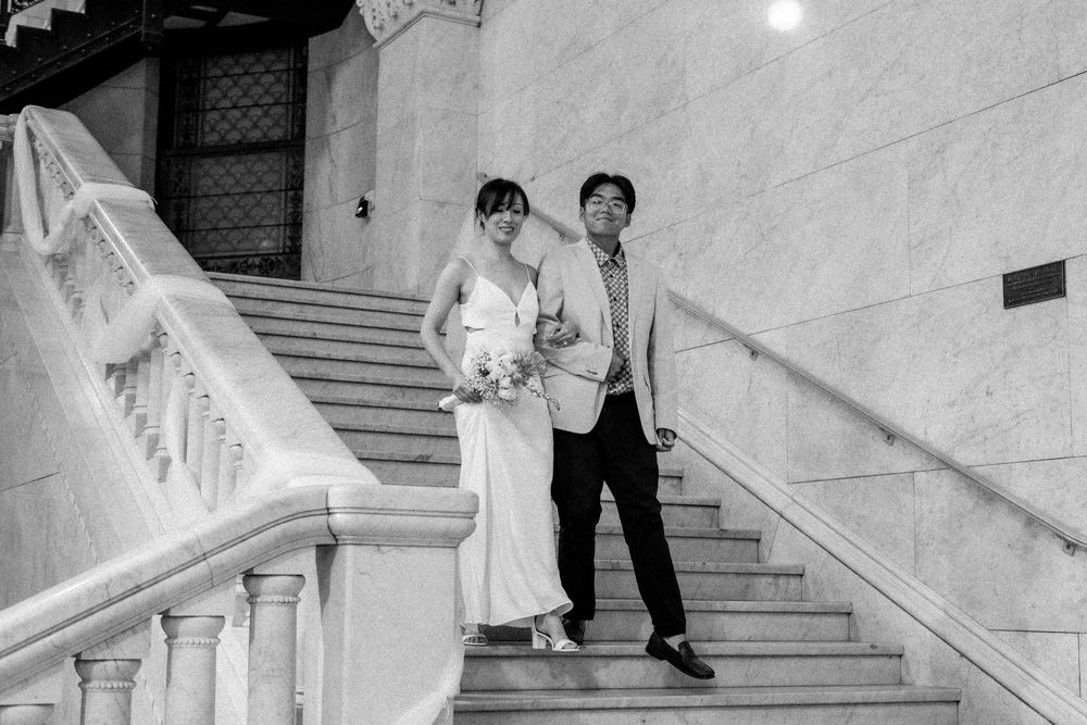 A couple poses on elegant white marble stairs in formal wedding attire during a romantic photo session.