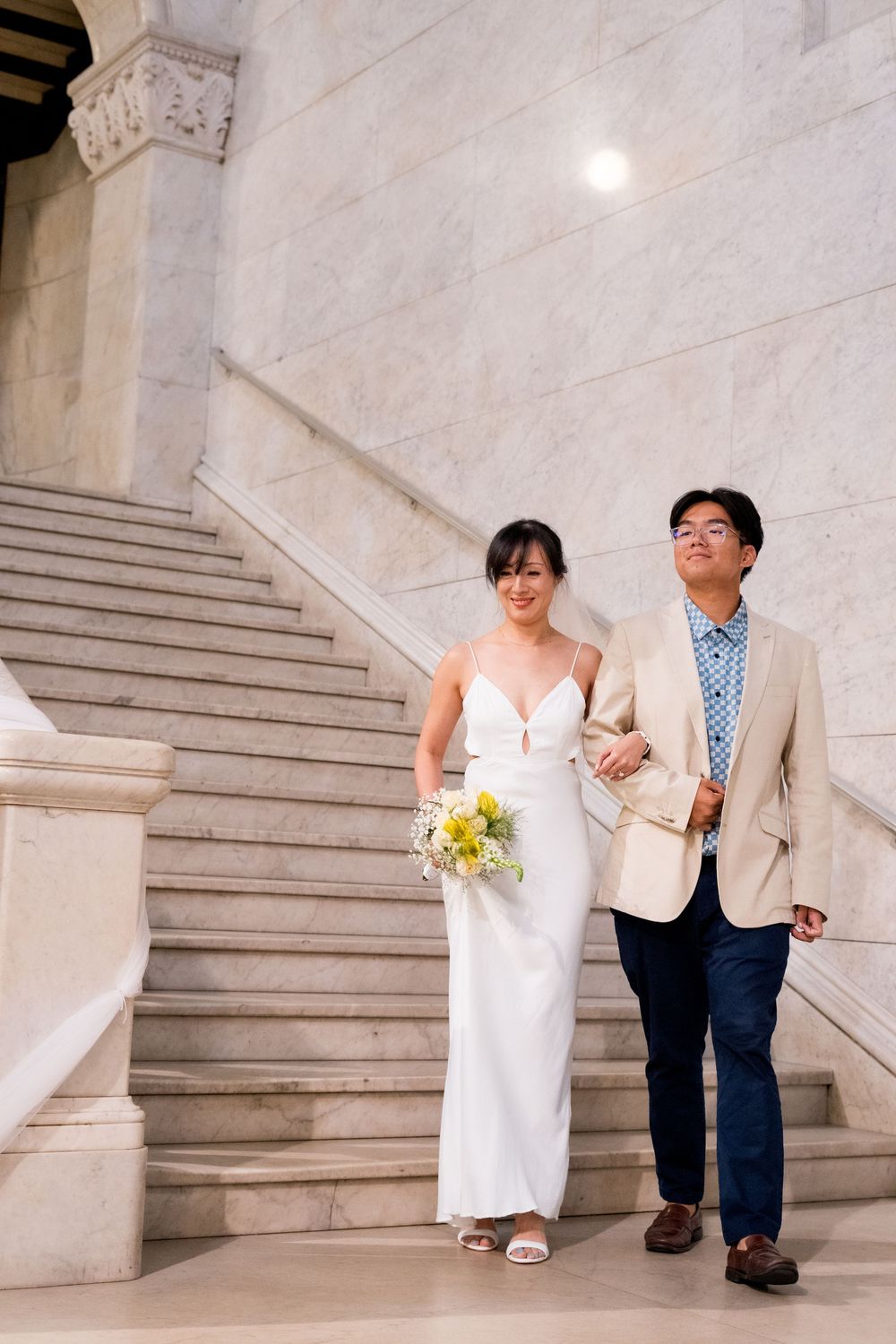 A couple shares a joyful moment on grand marble stairs in a classic architectural setting.