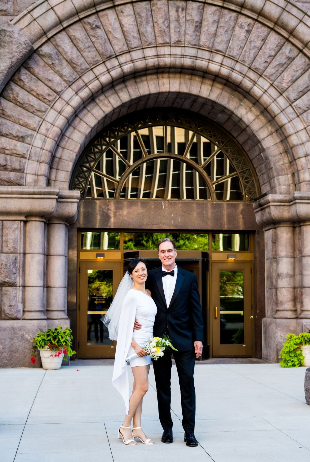 Newlyweds pose playfully in a series of photos under an elegant stone archway with decorative windows.