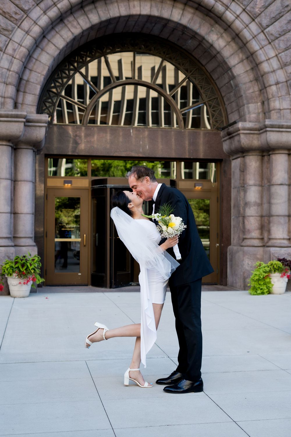 Romantic couple shares a dance pose under stone archways of a grand building entrance.