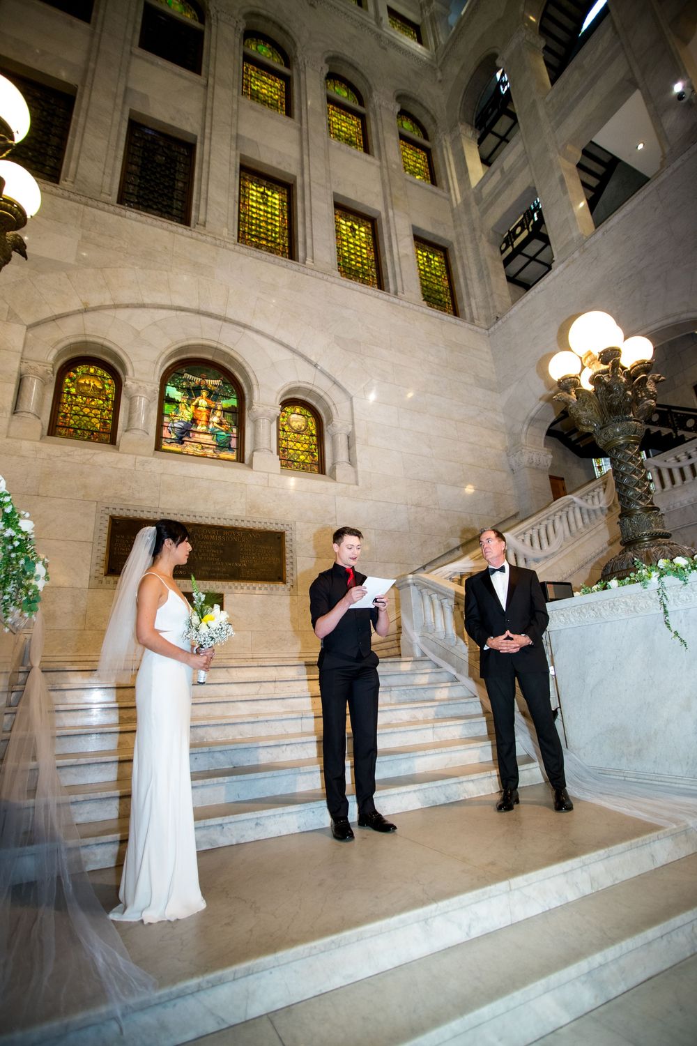 Elegant wedding portraits on grand marble staircase with stained glass windows in background.