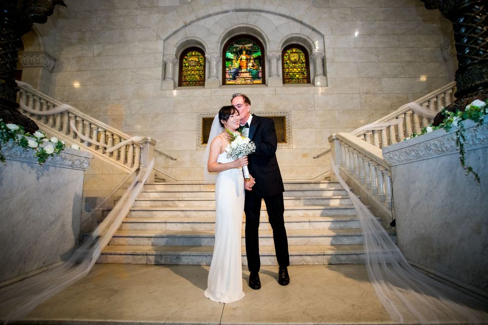 A romantic couple shares an intimate dance moment on an elegant stone staircase with stained glass windows in the background.