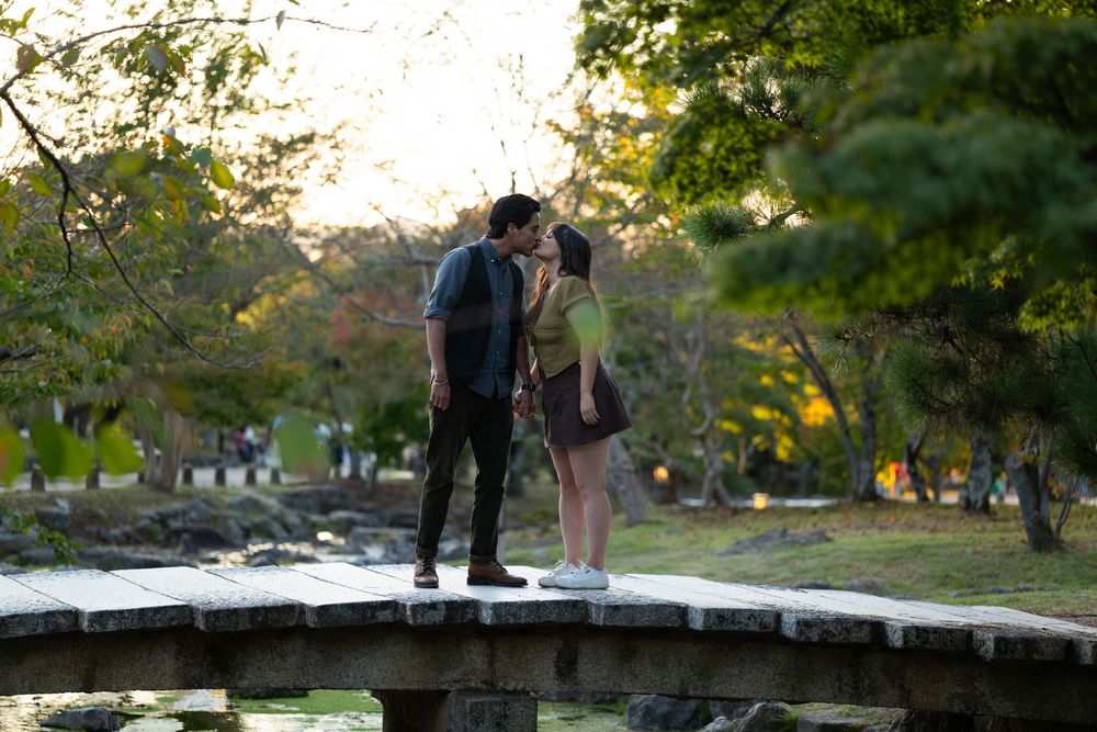 Couple sharing a romantic kiss on a stone bridge in a lush green park.