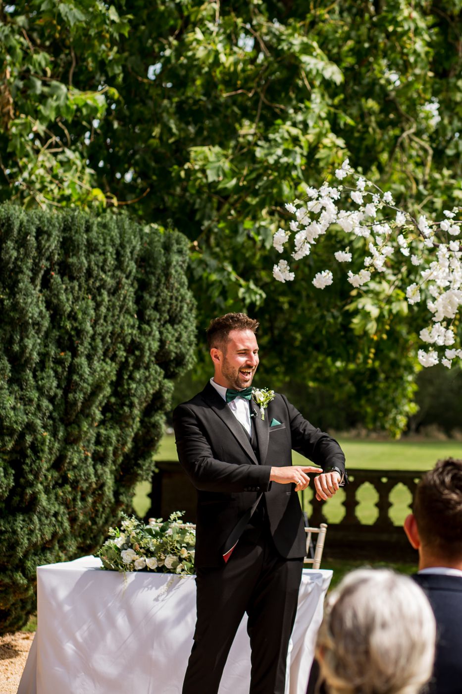 Two groomsmen share a lighthearted moment during an outdoor garden ceremony.