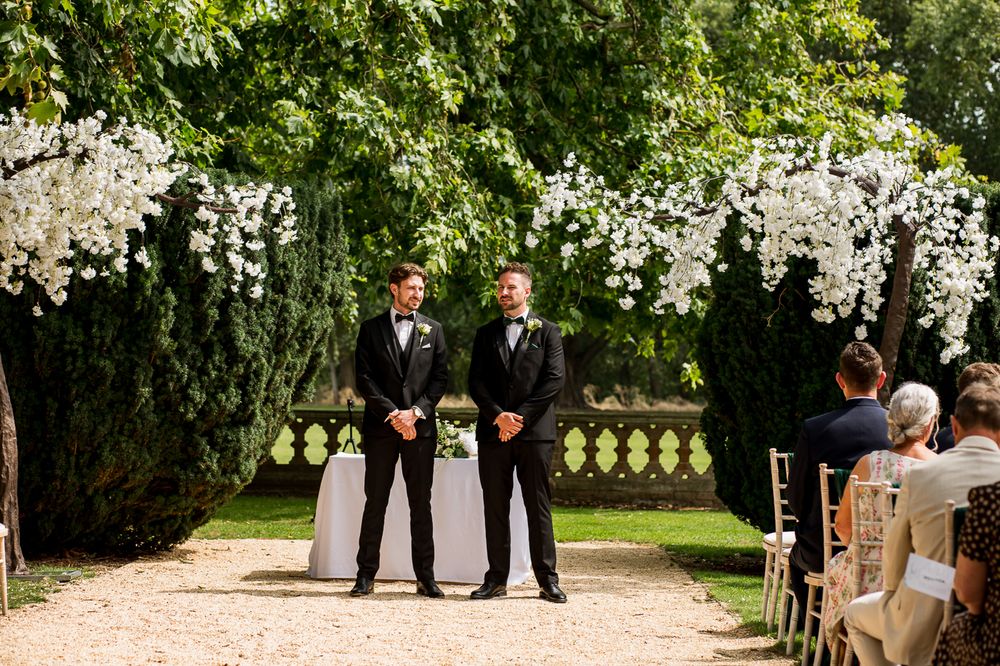 Outdoor wedding ceremony setup with white chairs and floral arrangements in a garden.