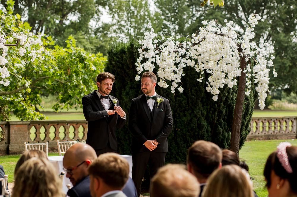 Wedding ceremony takes place in a beautiful garden setting with white floral decorations.