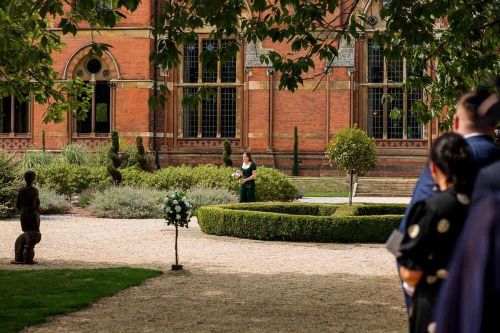 Guests seated in rows of chairs outside a grand Victorian Gothic style building for an outdoor event.