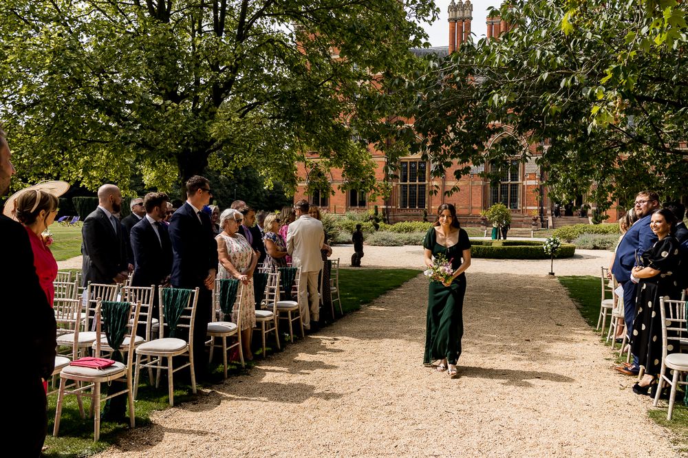 Tree-lined pathway with chairs arranged for an outdoor ceremony at a historic brick university building.