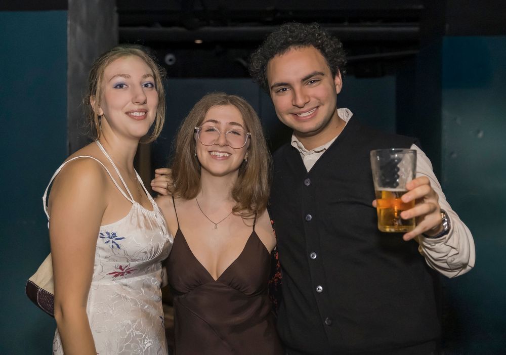 Group of friends posing together at a dimly lit bar or party venue with drinks in hand.