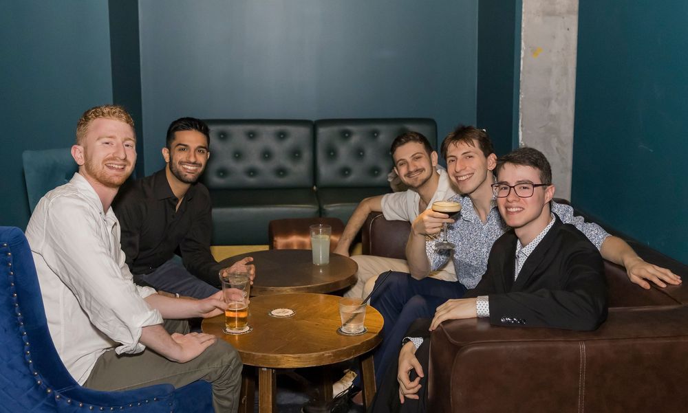 A group of people socializing and enjoying drinks together at a dimly lit bar or restaurant.