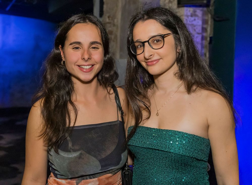 Two people in formal attire pose together at an event with blue lighting in the background.