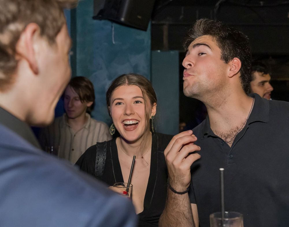 Close up shot of people smiling and socializing in a dark indoor setting.