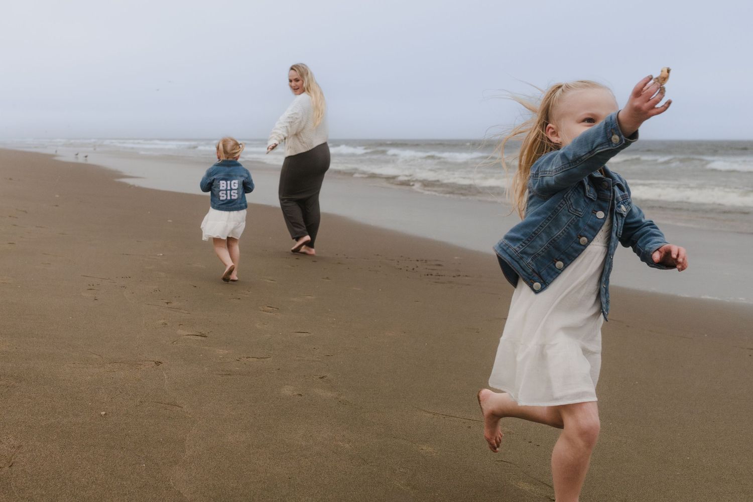 People enjoying a playful moment on a sandy beach with waves and cloudy skies in the background.