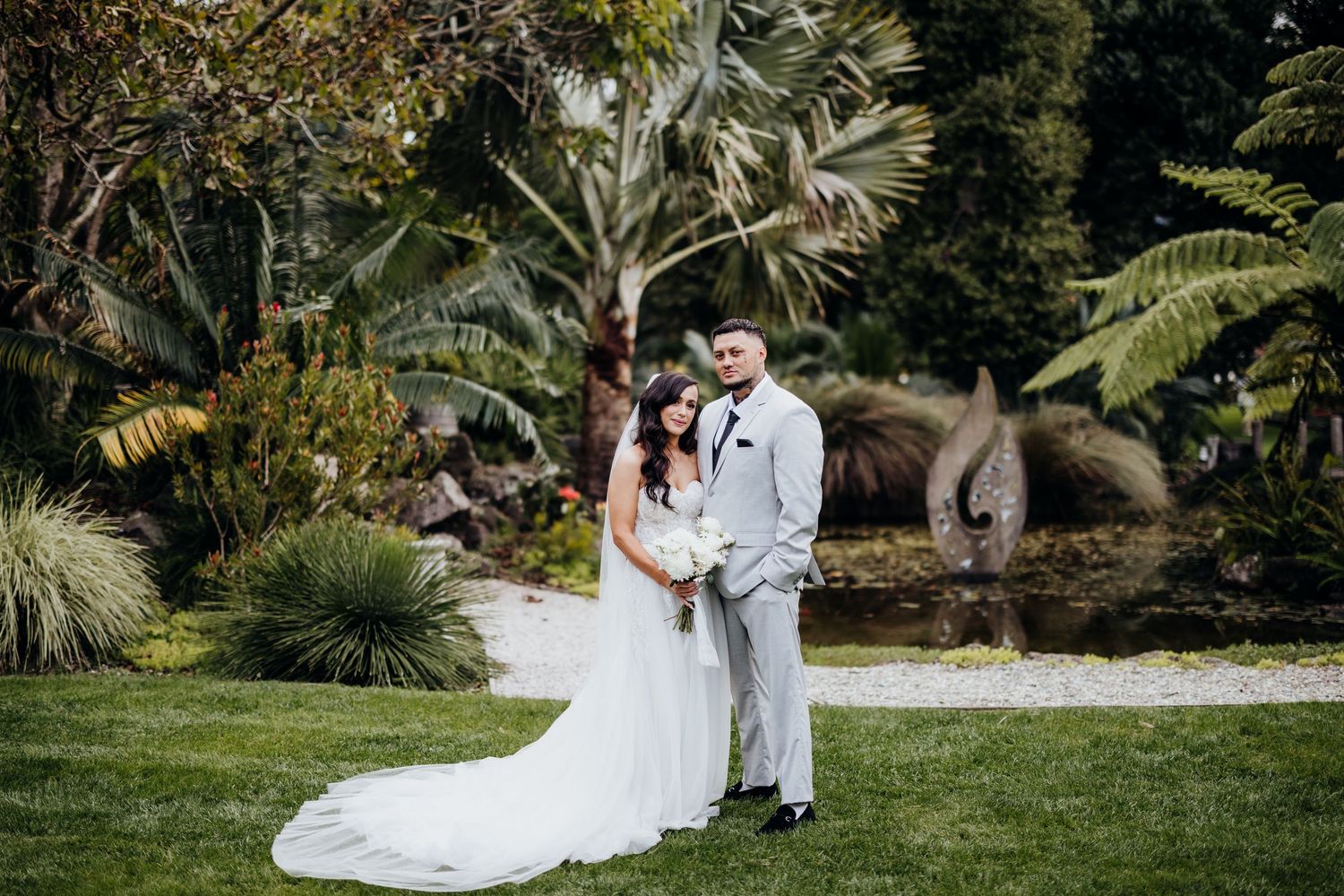 White chairs and a decorative arch are arranged for an outdoor wedding ceremony in a lush garden setting.