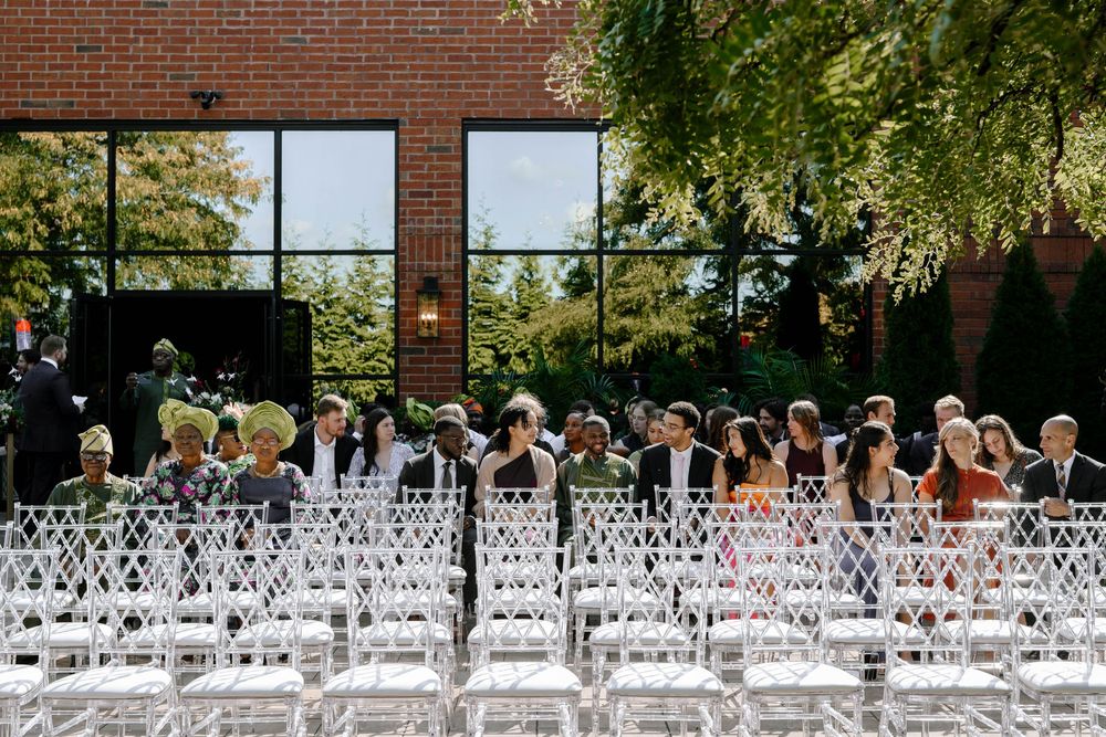 White chairs arranged in rows for an outdoor wedding ceremony against a brick building with large windows.