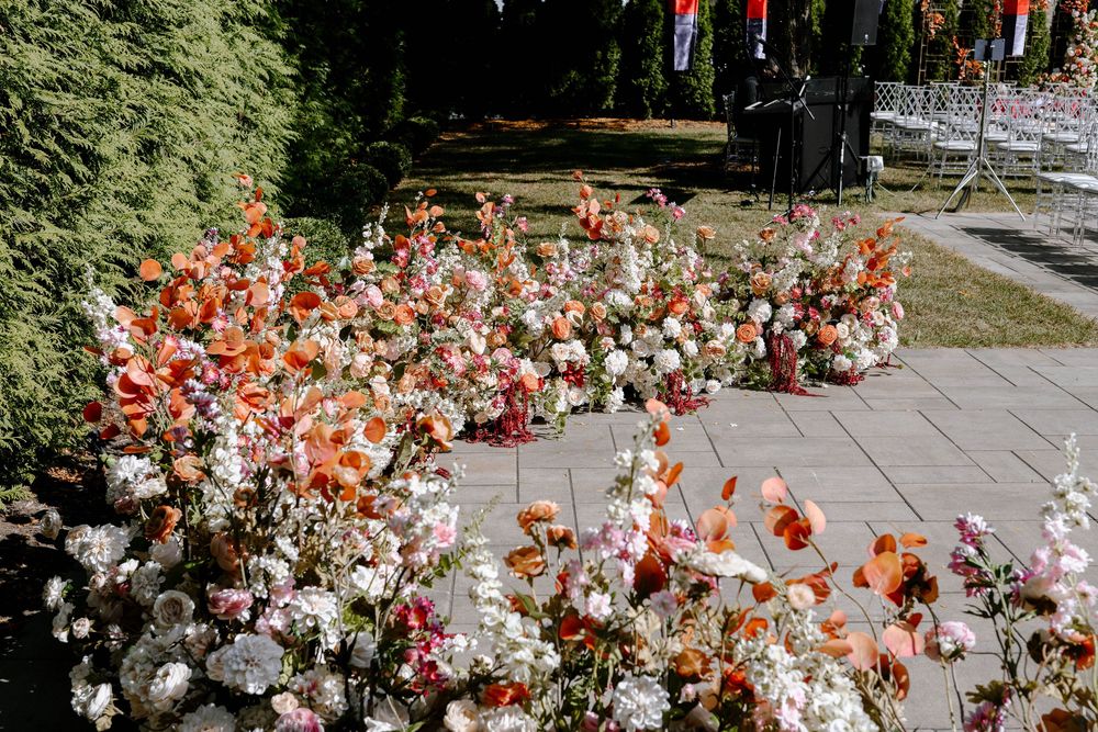 Beautiful orange and white floral arrangements decorate an outdoor wedding venue with string lights overhead.