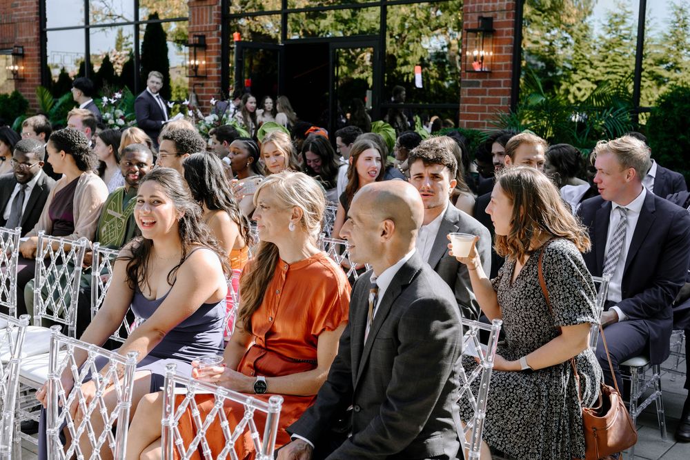 Wedding guests gather on an outdoor patio with brick walls and large windows during a celebration event.
