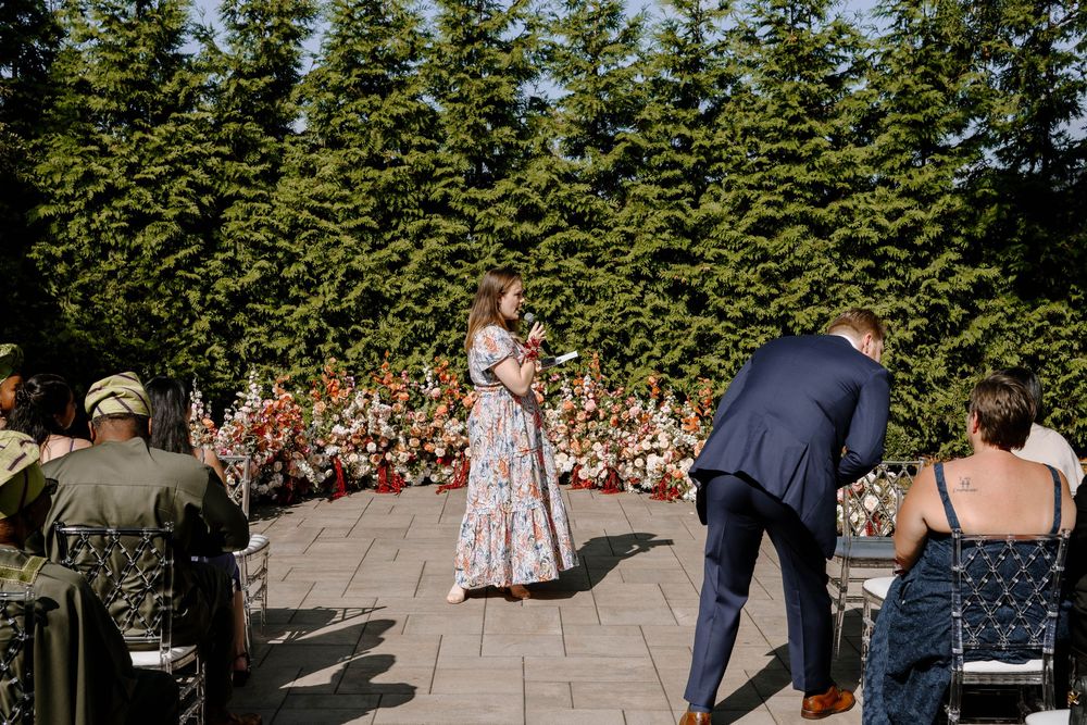 Outdoor wedding ceremony with guests seated in rows among lush greenery and trees.