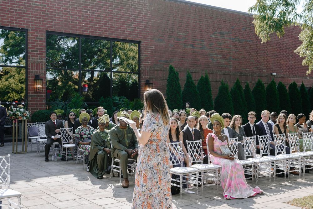 Panoramic view of an outdoor wedding ceremony setup with white chairs and brick building backdrop.