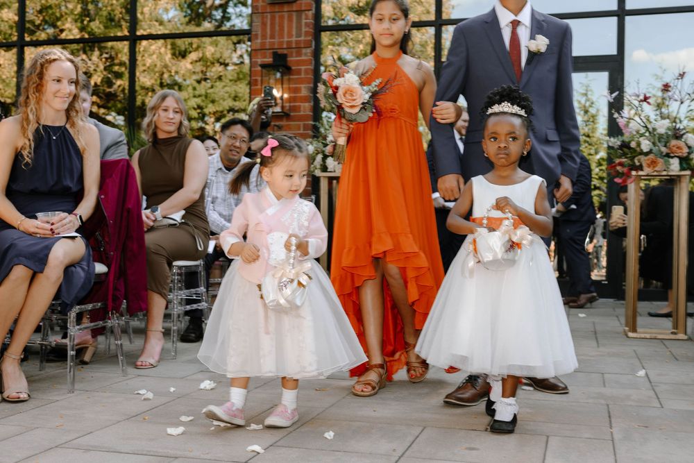 Wedding party members gather on stone steps surrounded by elegant floral decorations in orange and white.