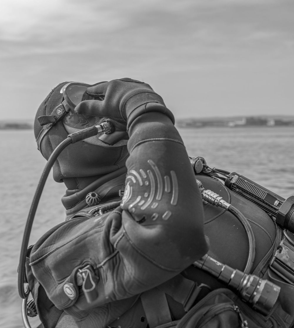 A close-up black and white shot of a scuba diver's equipment and wetsuit against an ocean backdrop.