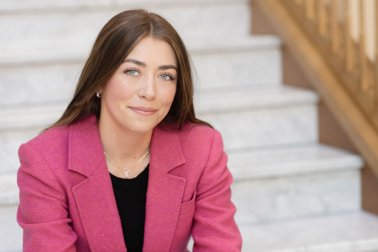 Professional portrait on stairs wearing bright pink blazer.