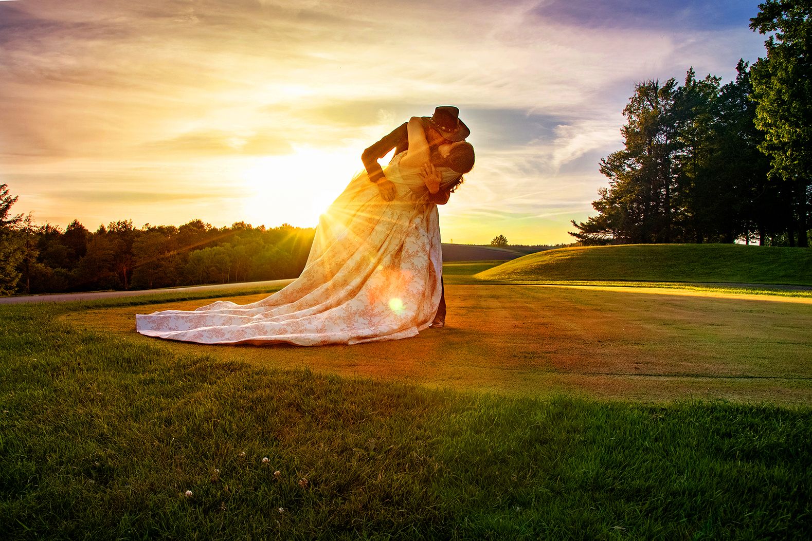 Couple sharing a romantic dip kiss in wedding attire at golden sunset on lush green golf course.