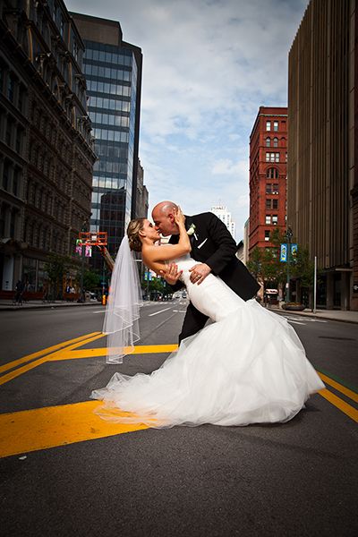 A romantic wedding photo on a city street with historic buildings and modern architecture in the background. (Downtown Rochester New York)