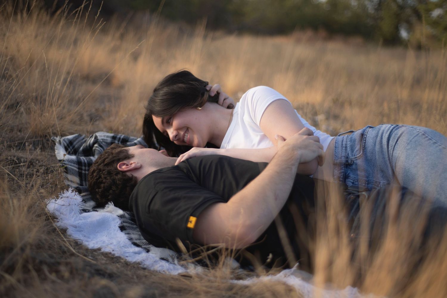 Romantic couple lying together in golden dry grass field, sharing an intimate moment outdoors.