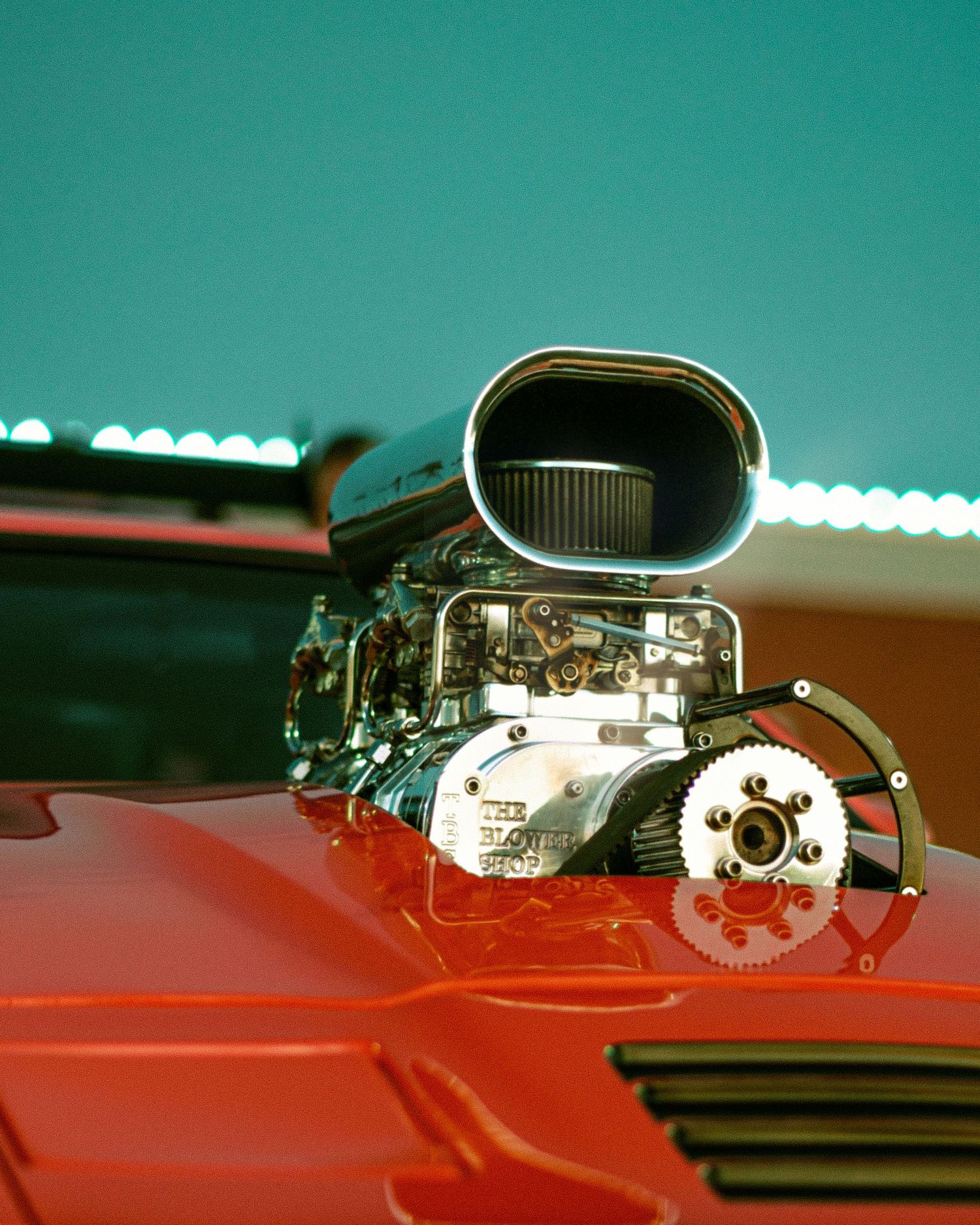 Chrome supercharger engine detail on a red classic car hood.