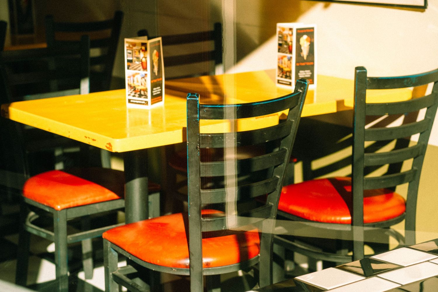 Restaurant interior with yellow tables and red chairs in warm lighting.