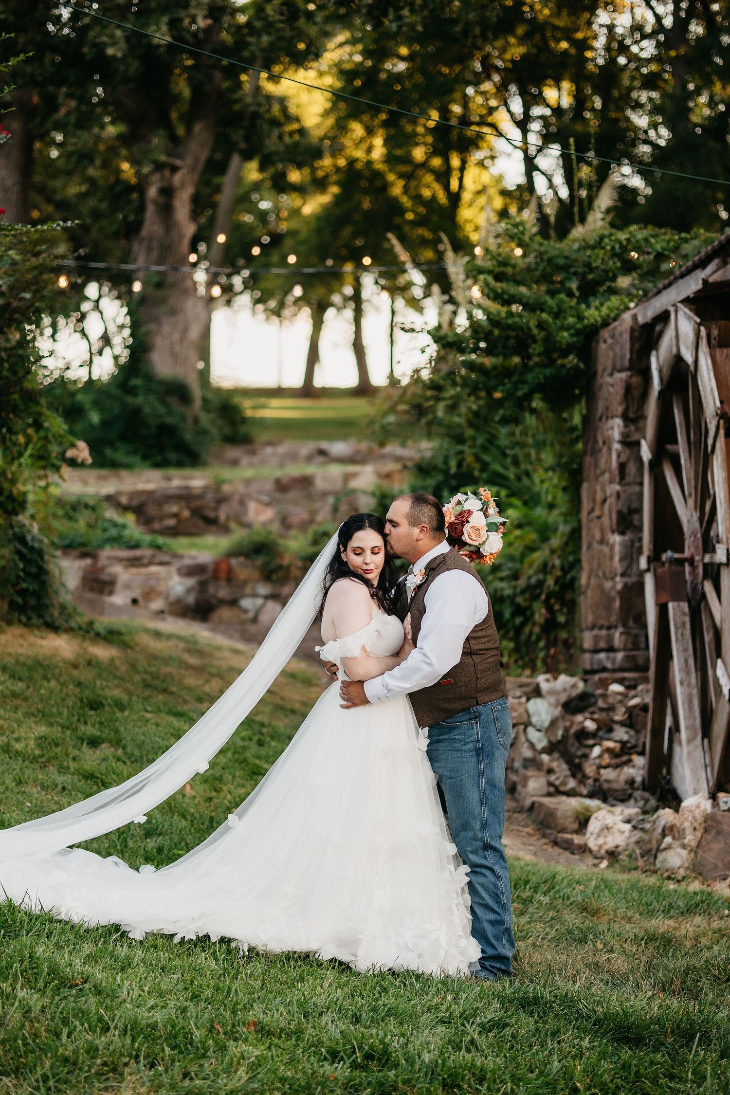 A romantic wedding photoshoot in a scenic outdoor setting with stone walls and trees.