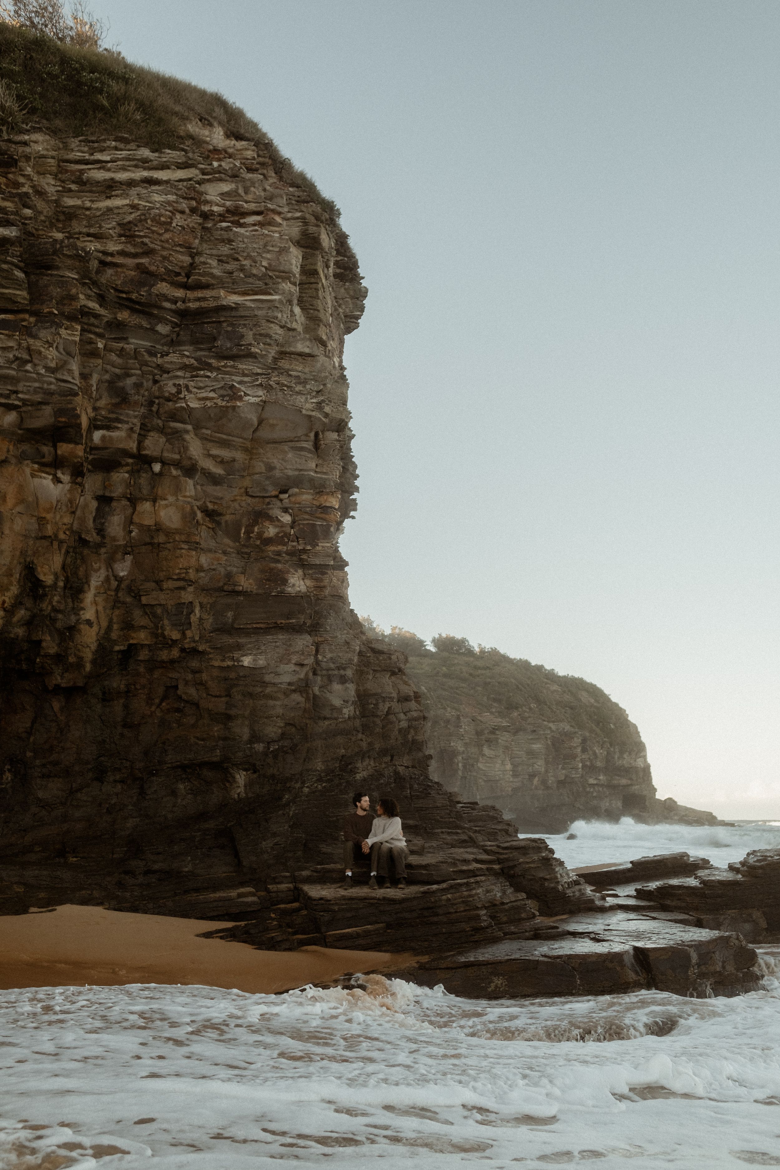 Couple sitting on rocks on a sandy beach.