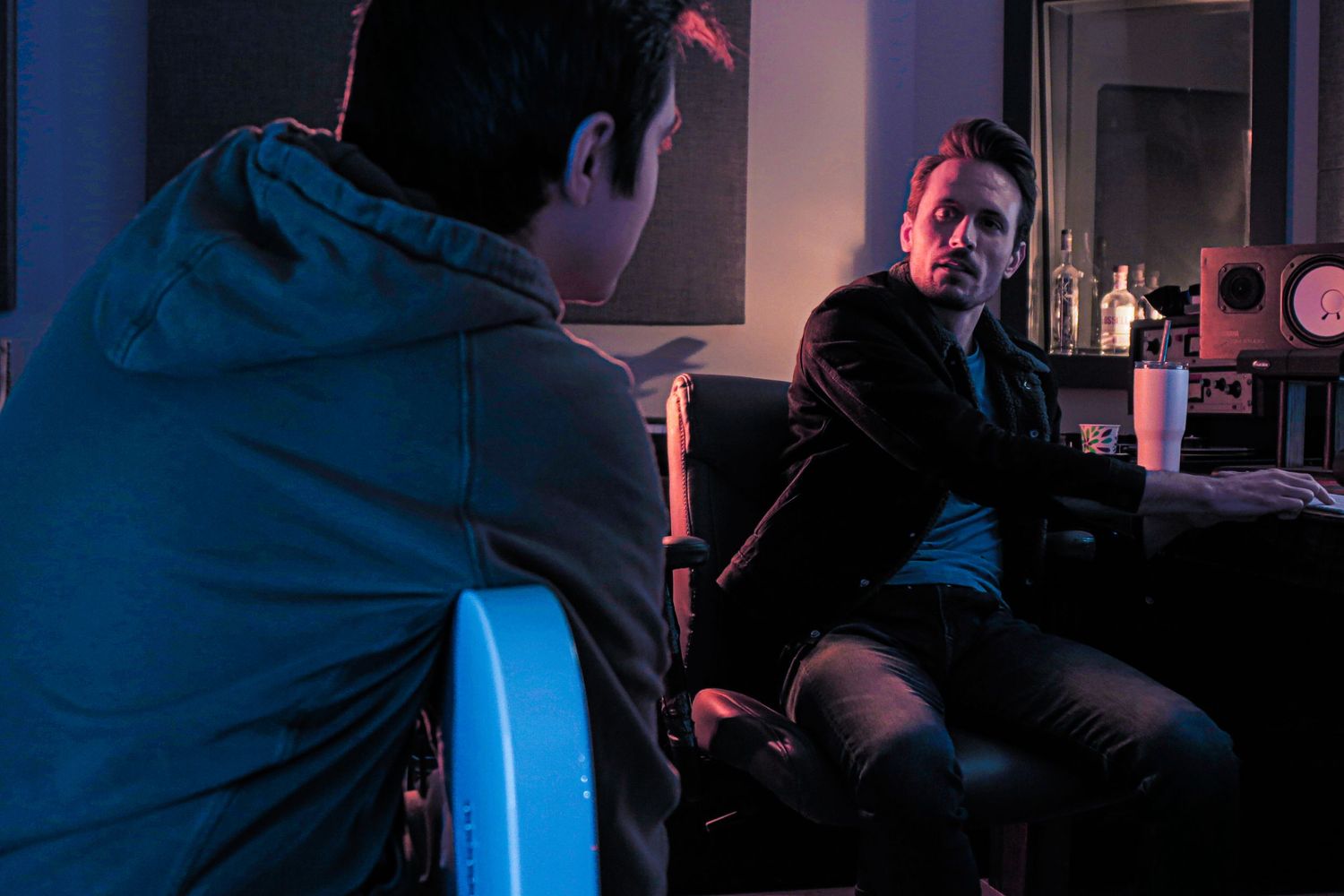 Dimly lit interview setup in a studio with dramatic blue and red lighting.
