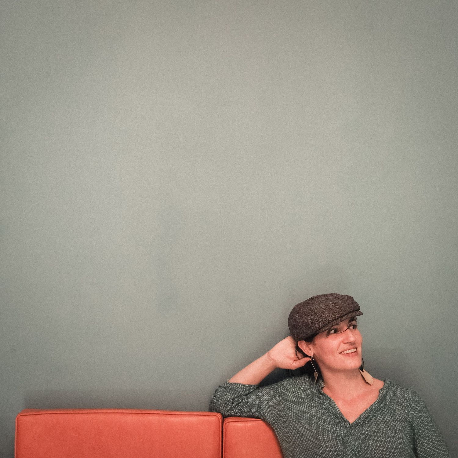 Person in a green shirt leaning against a grey wall with a thoughtful expression.