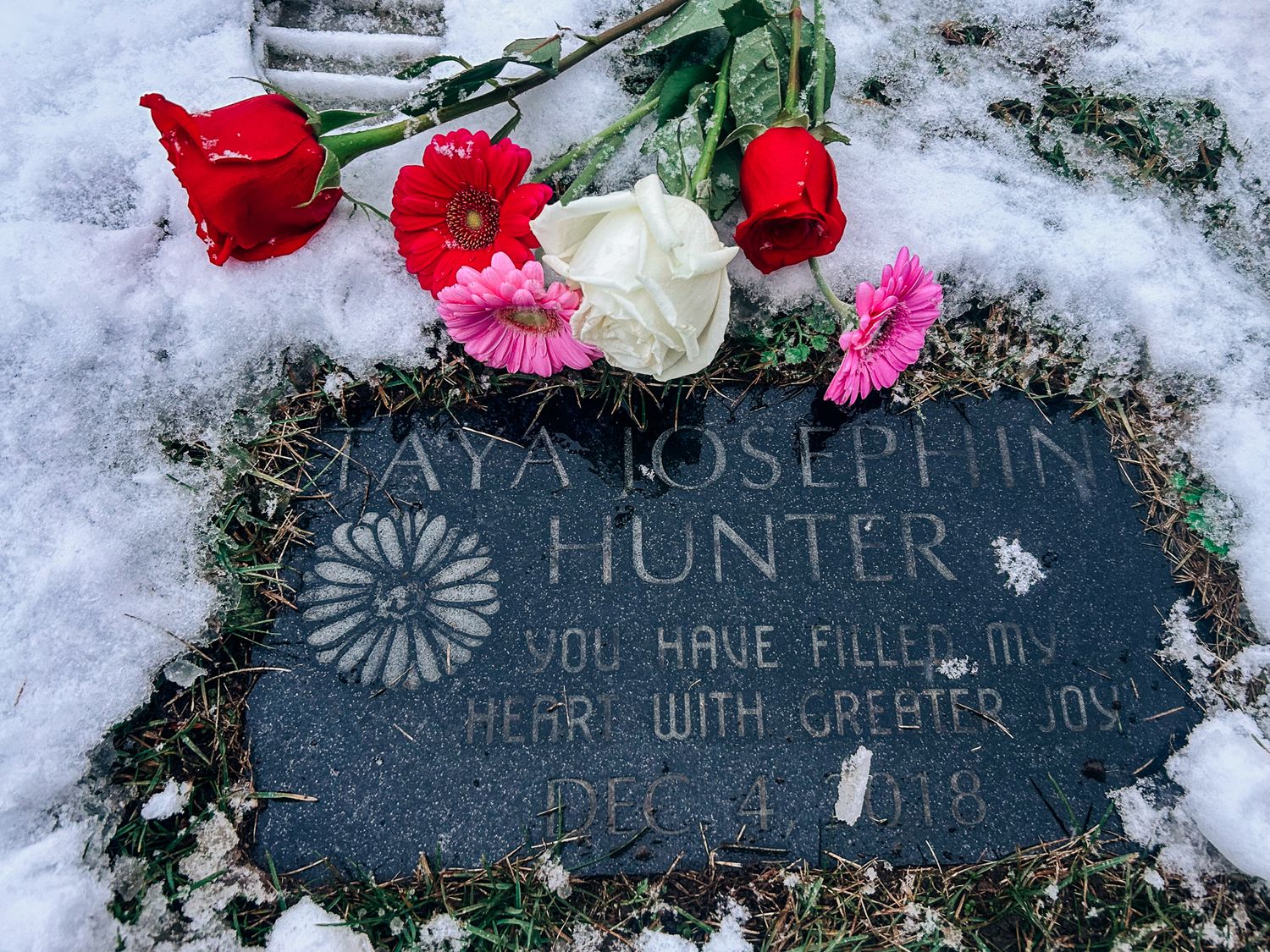 Colorful roses placed on a snow-covered memorial stone with engraved message.