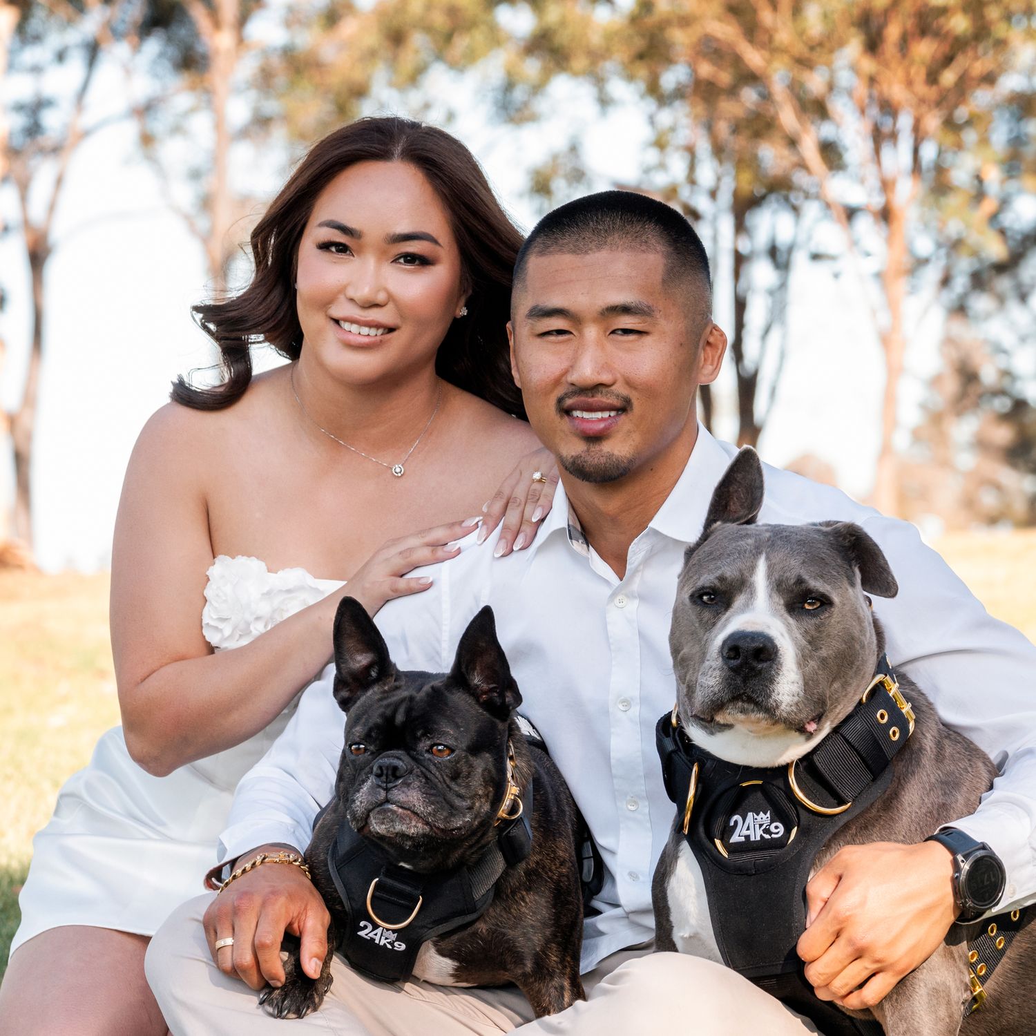couple smiling towards the camera while sitting on the ground and hugging their dogs during an elopement photoshoot in Sydney