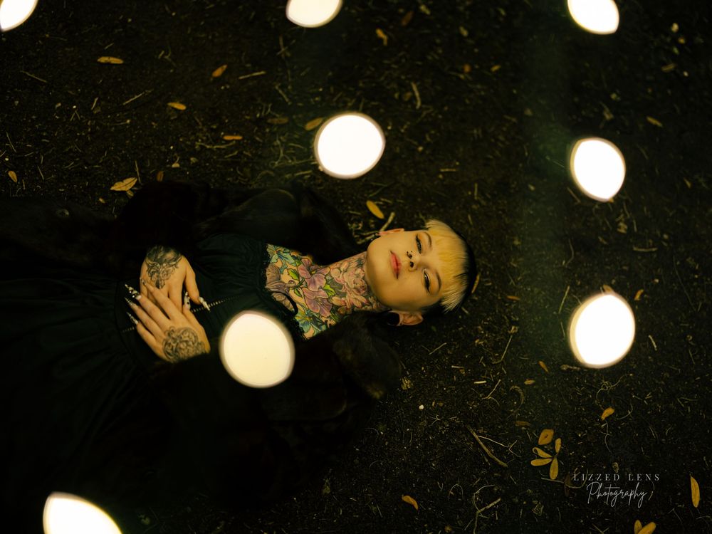 Tattooed person lies among glowing circular lights on dark ground in an artistic night photography composition.