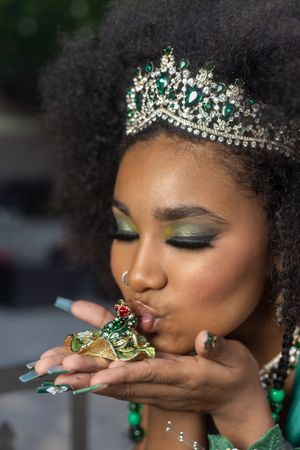 Close-up shot of sparkly tiara and emerald makeup with playful kiss pose.