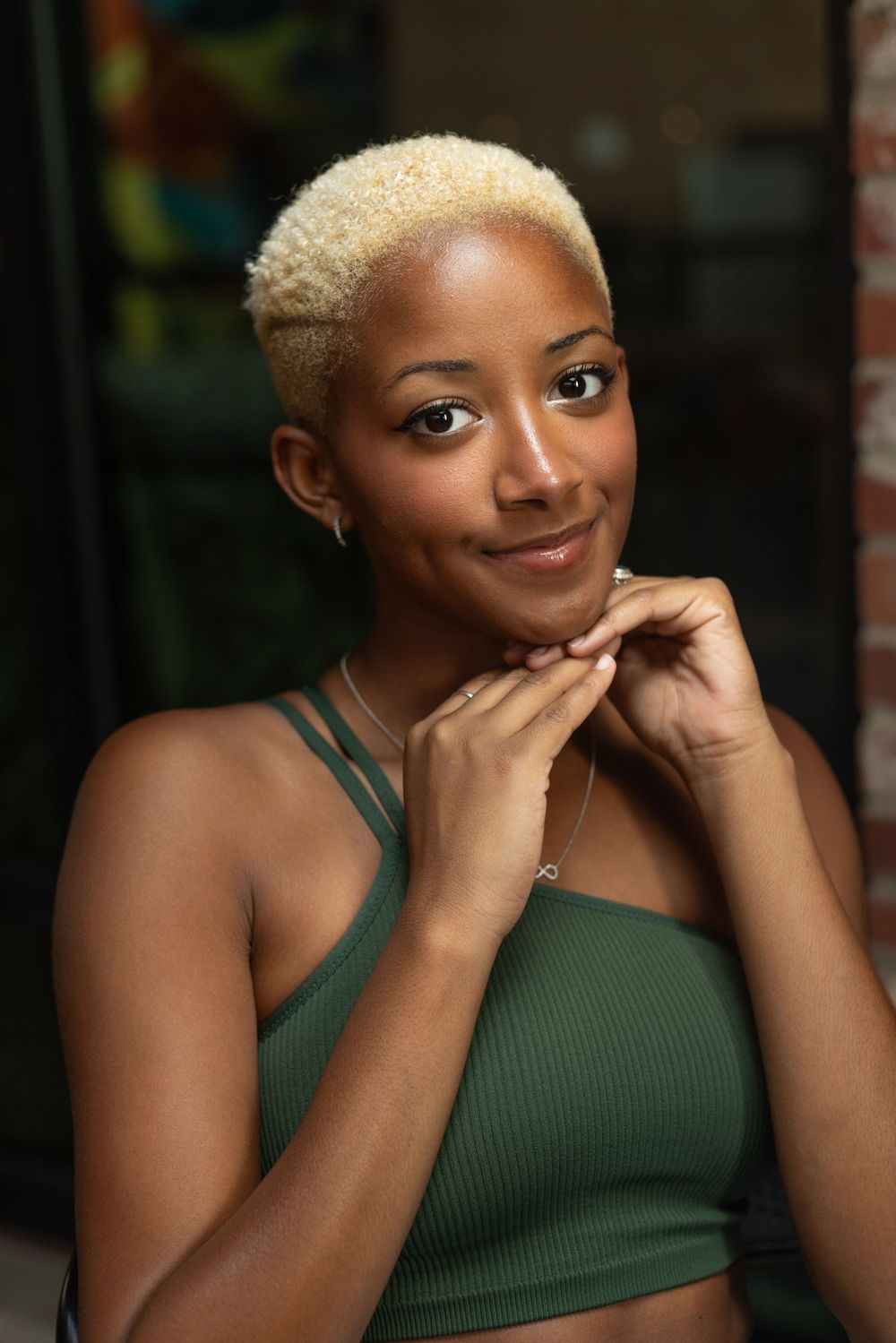 Portrait of someone with short platinum hair wearing a green top in a natural outdoor setting.