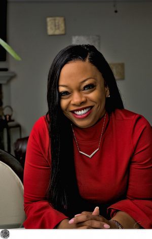 Professional headshot of woman in red sweater with chevron necklace and bright smile.