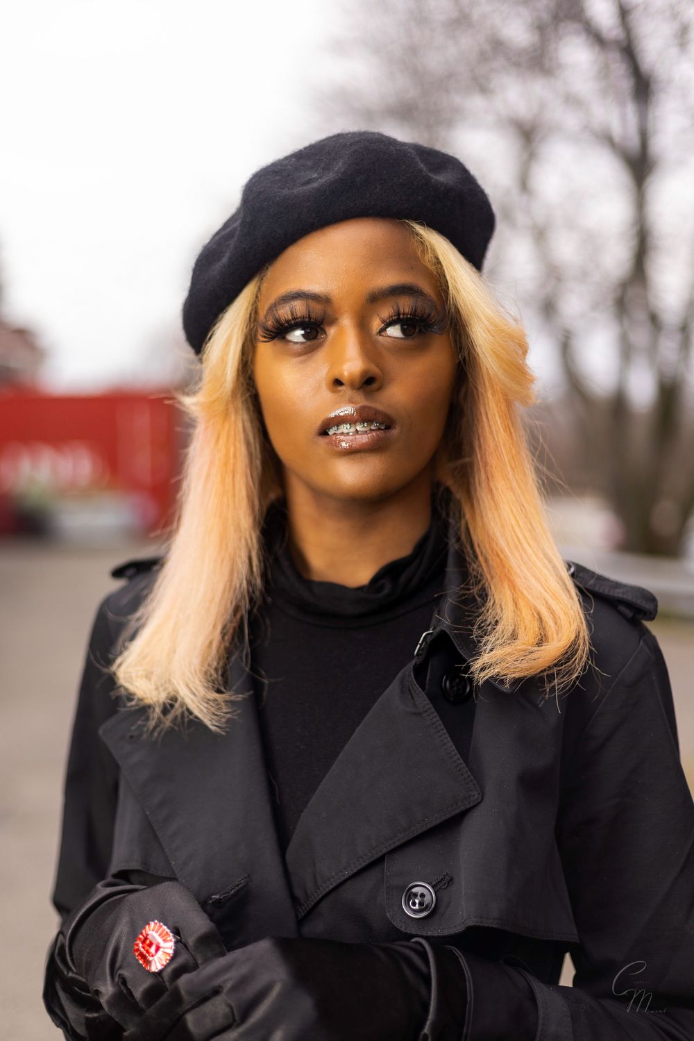 Stylish winter fashion portrait featuring black beret, coat and gloves against blurred outdoor background.