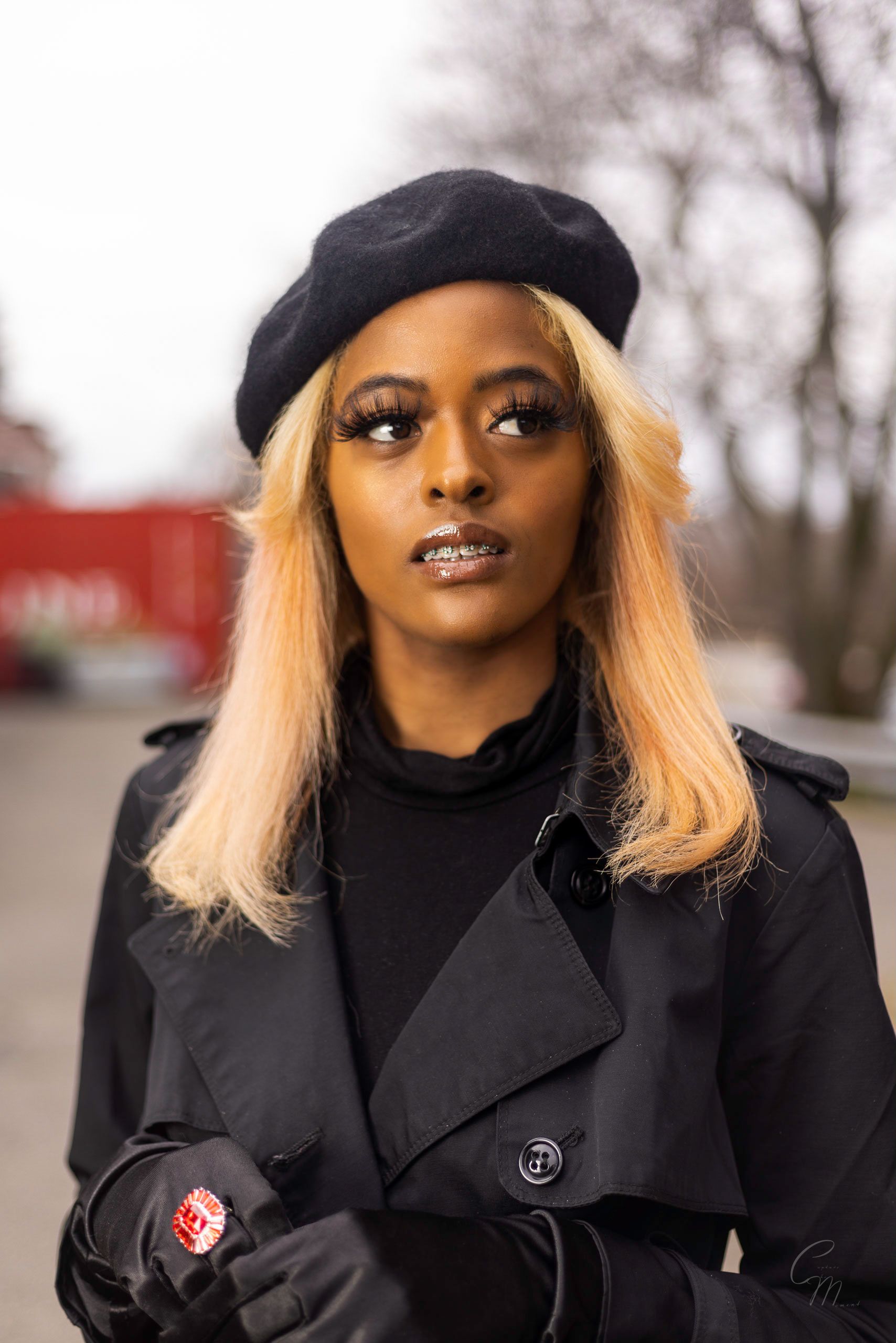 Stylish winter fashion portrait featuring black beret, coat and gloves against blurred outdoor background.
