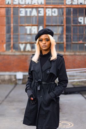 Urban fashion photo with black trench coat and beret against industrial building backdrop.