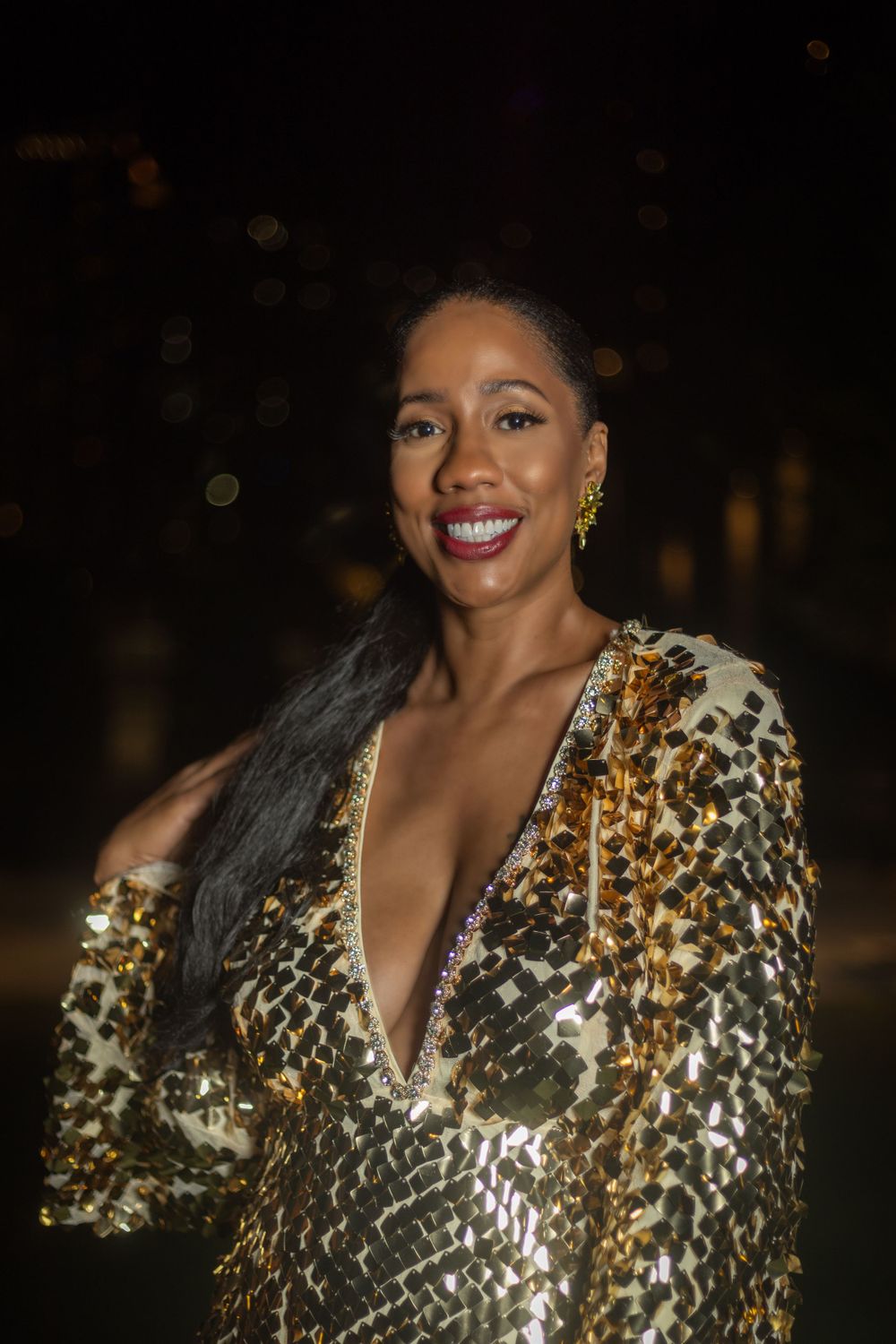 Evening portrait of someone wearing a sparkly gold sequined dress against a dark background.