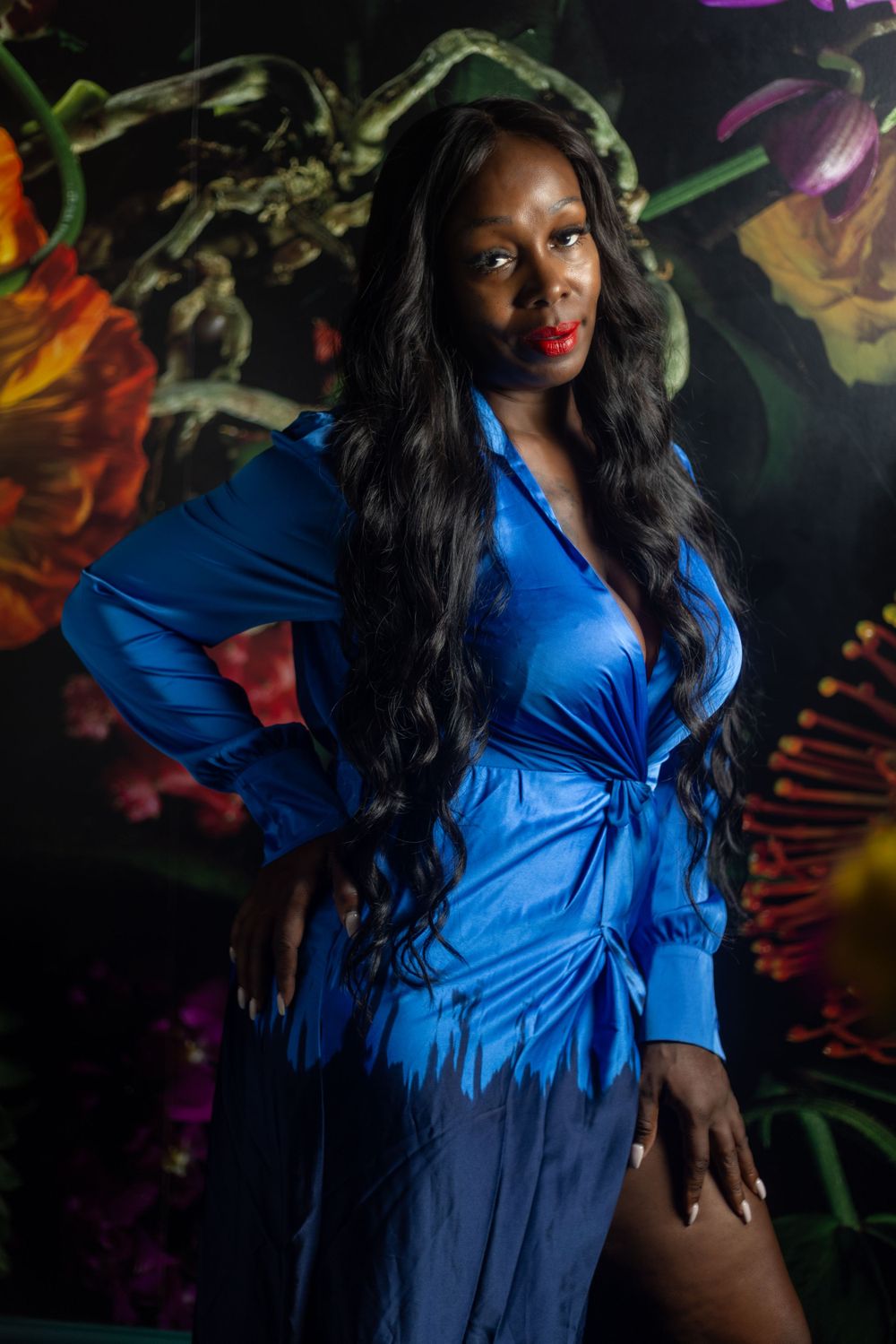 Portrait of someone in a flowing blue dress posing against a colorful abstract mural background.