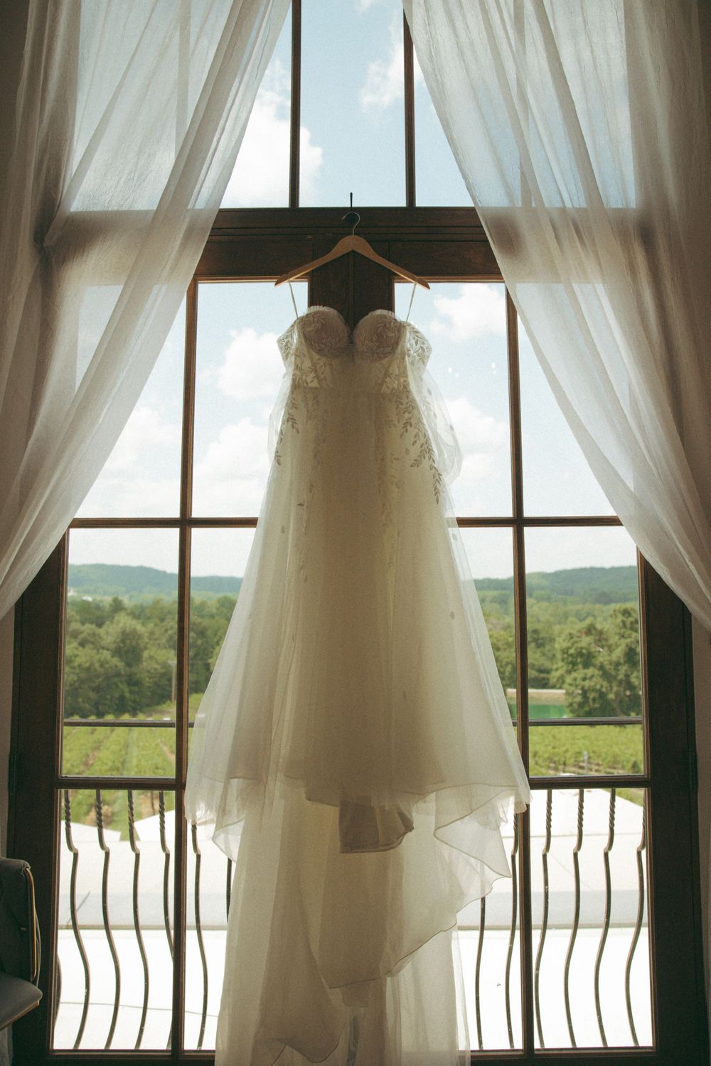 Elegant white wedding dress hanging in window frame with scenic mountain backdrop.